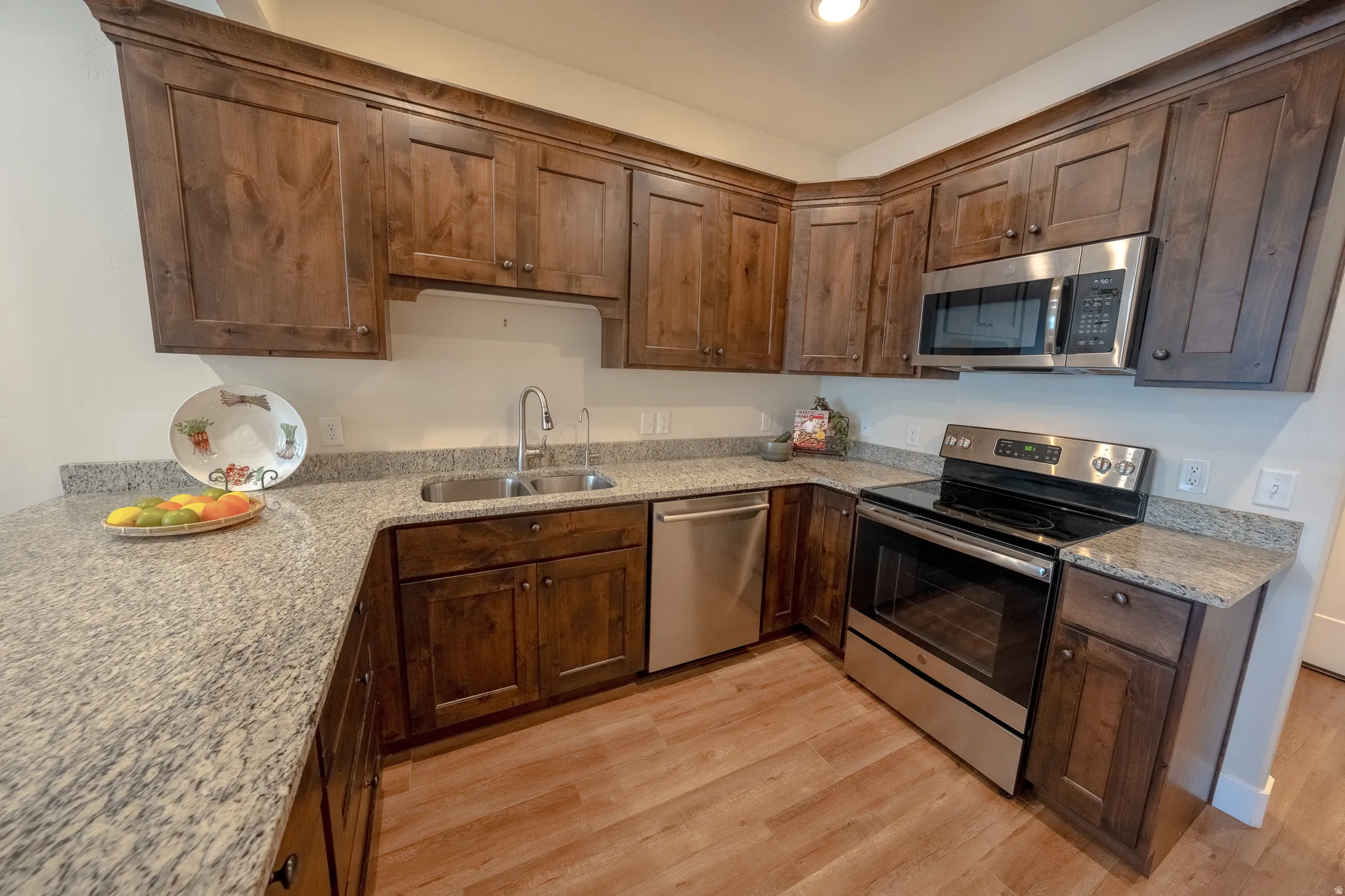 U-shaped kitchen with wood-finish flooring, light-toned countertops, wood cabinetry, and stainless-steel appliances