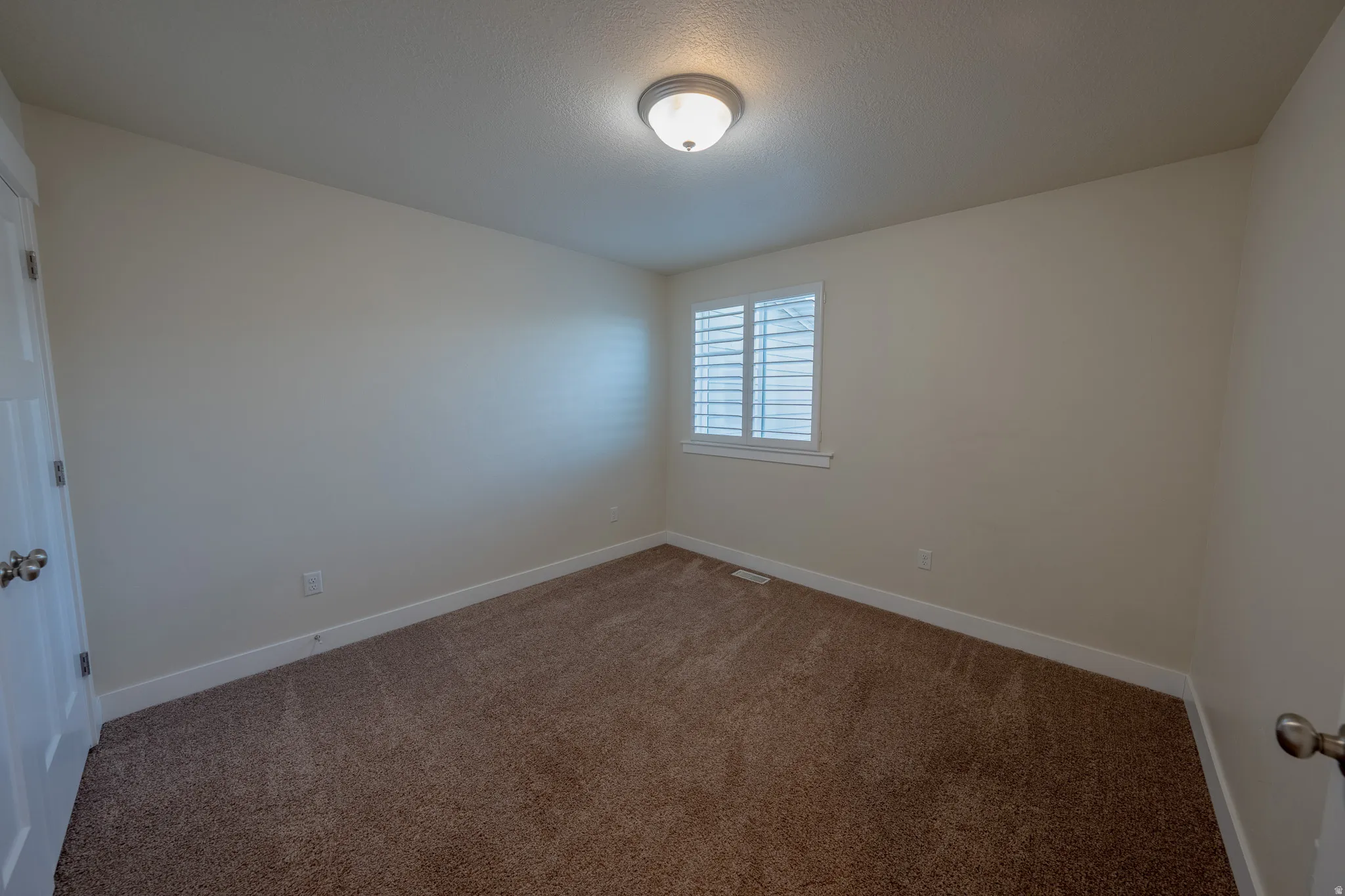 Neutral wall paint, plush carpeting, window with plantation shutters, and a semi-flush mount ceiling light fixture