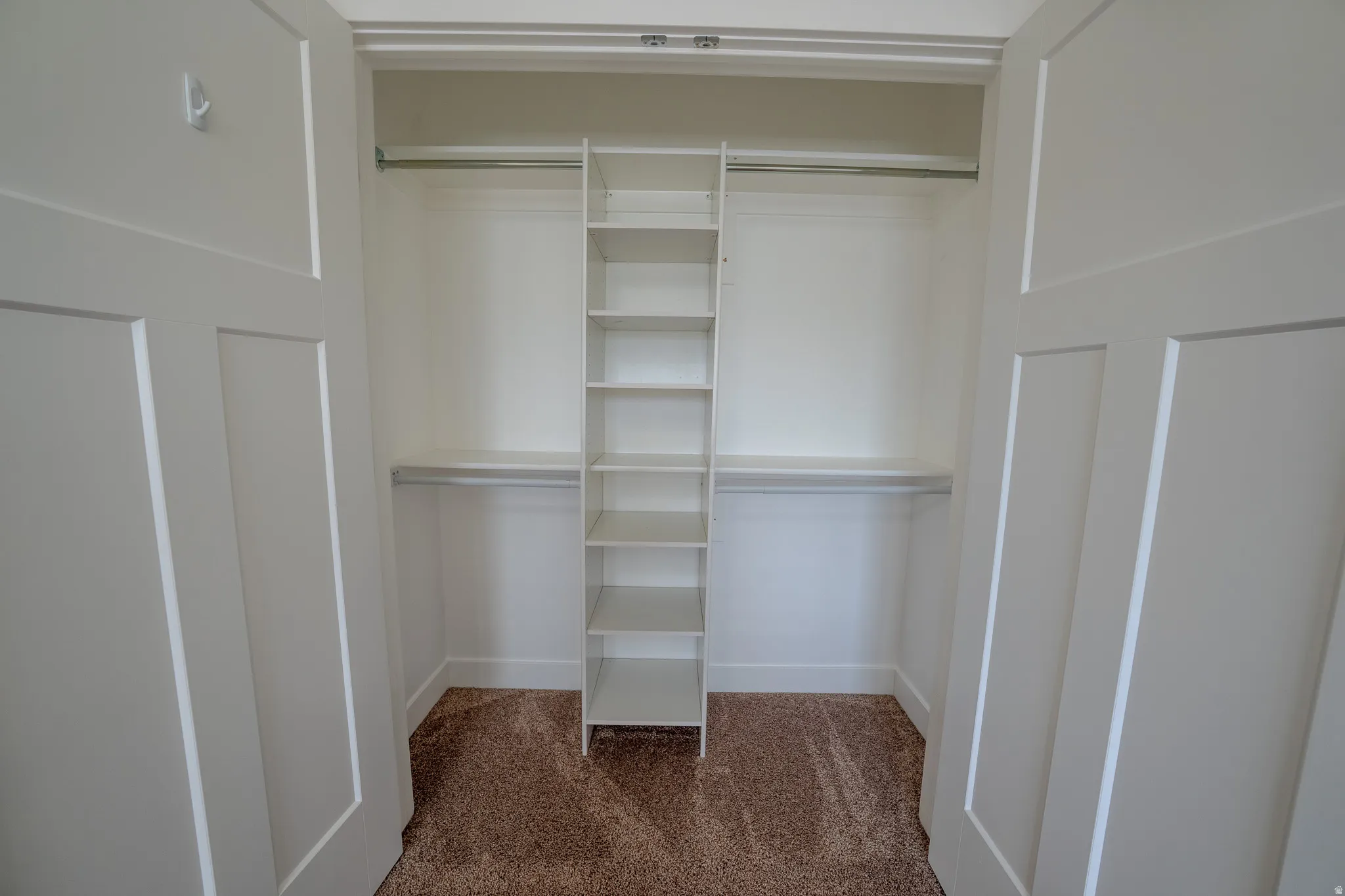 Built-in closet shelving, dual hanging rods, soft carpet flooring, and white paneled doors