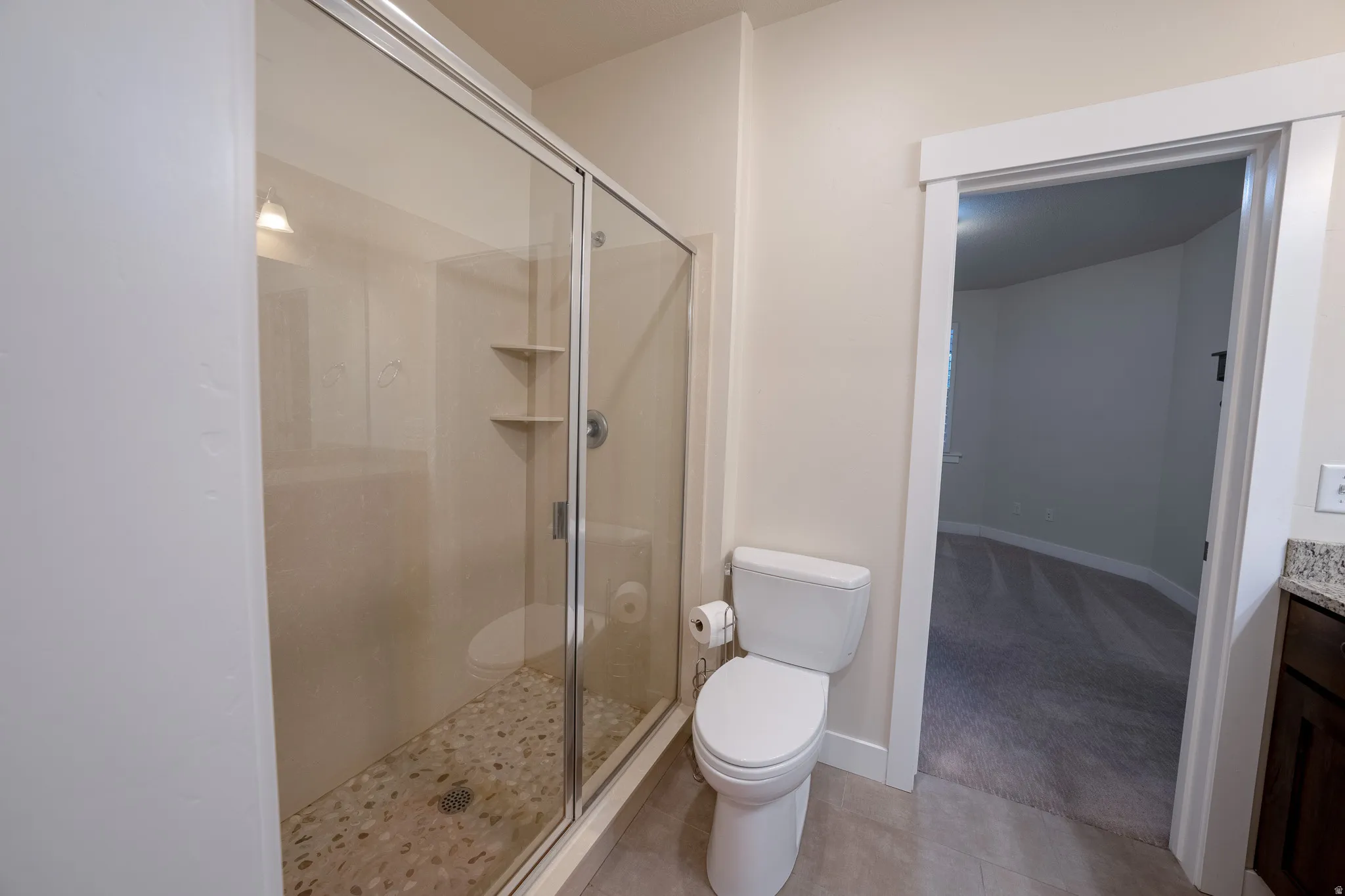 Walk-in shower with clear glass enclosure, pebble-tile flooring, and built-in shelving