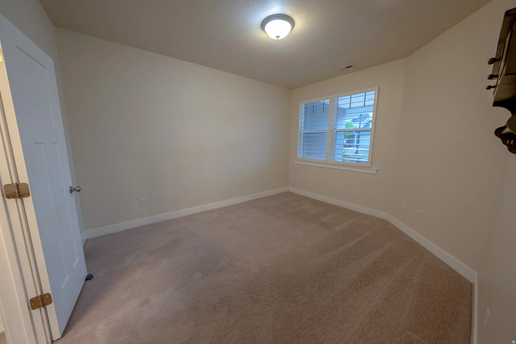 Neutral wall tones, recessed window with plantation shutters, ceiling-mounted light fixture, and carpeted flooring