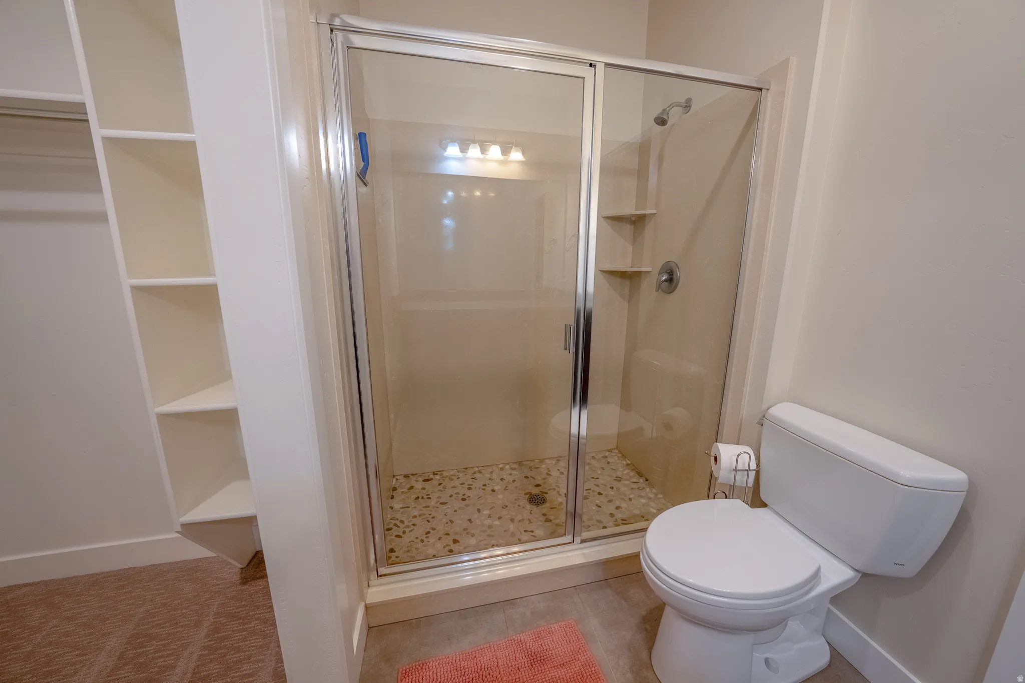 Glass-enclosed shower with a pebble-finish floor, built-in shower shelving, and a white toilet