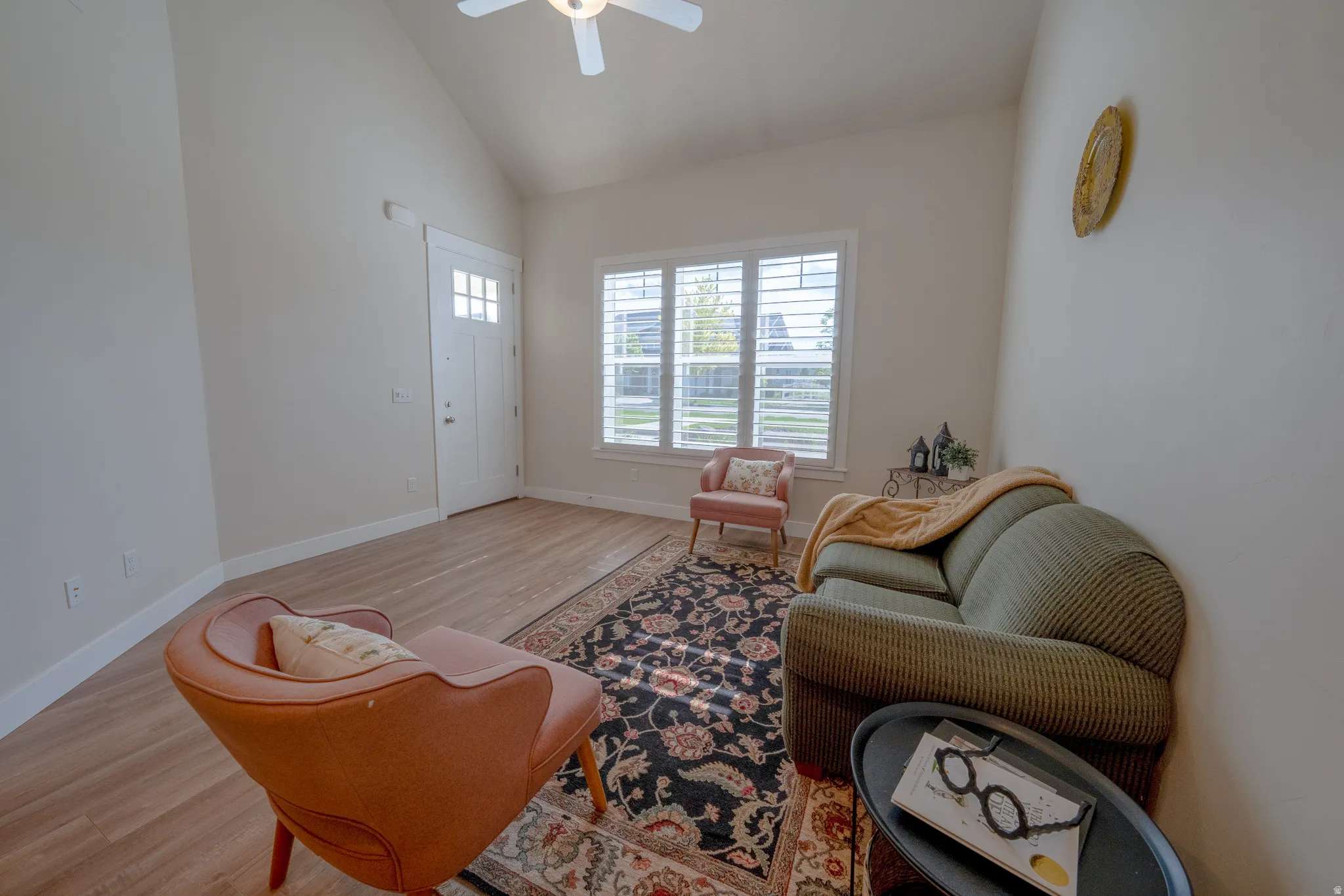 Vaulted ceiling with a ceiling fan, white paneled entry door with multiple lites, wood-finish flooring, and window with white plantation shutters