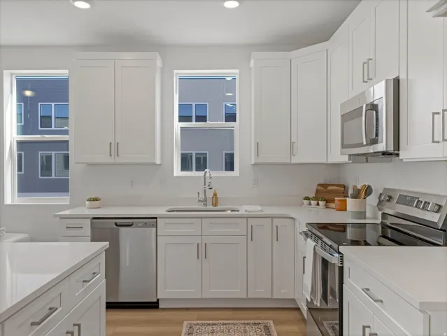 Kitchen featuring white shaker-style cabinetry, stainless steel appliances, a white solid-surface countertop, and wood-finish flooring