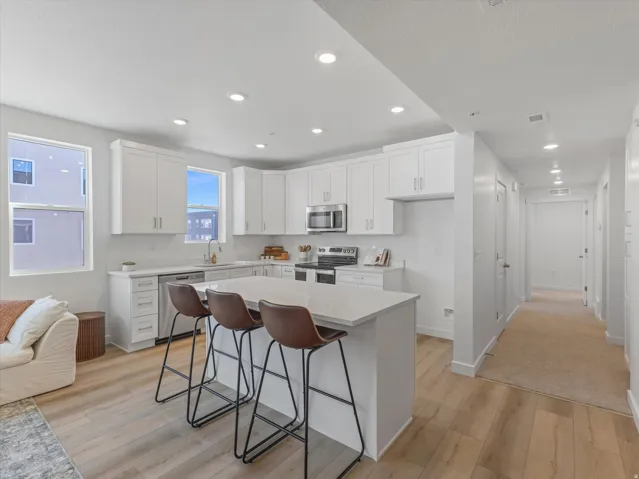 Contemporary kitchen featuring white cabinetry, stainless steel appliances, a center island with countertop seating, and light wood-finish flooring