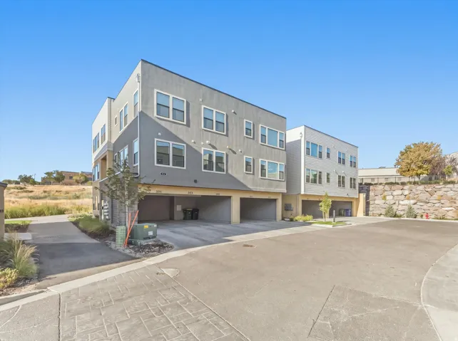 Contemporary multi-level residences featuring stucco and horizontal siding, individual garage entrances, and a stone retaining wall