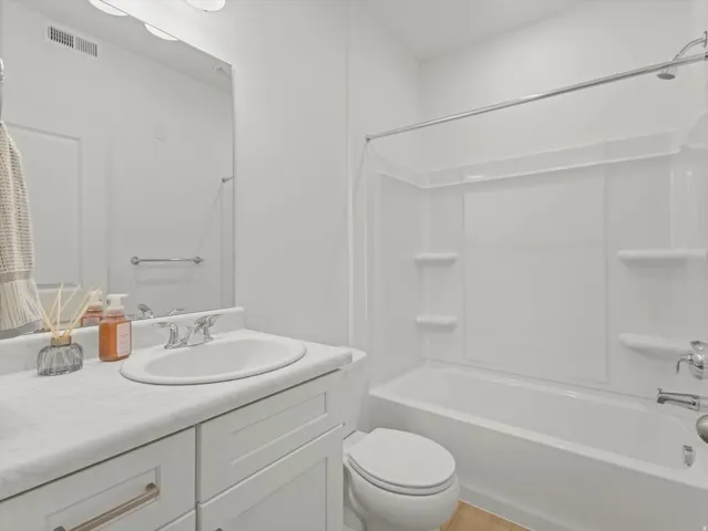 Integrated bathtub and shower combination, white vanity with an integrated sink, polished chrome faucet, and bronze-finish hardware