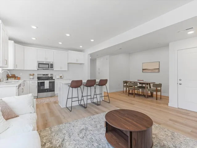 White shaker cabinetry with stainless steel appliances, central island with seating, recessed lighting, and wood-finish flooring