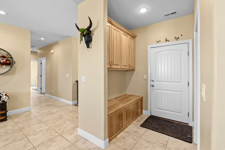 Entryway featuring tile flooring, built-in wooden storage bench, wooden upper cabinetry, and a paneled white door