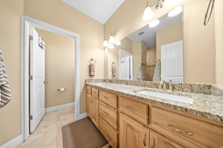 Dual vanity with granite countertop, integrated sinks, chrome fixtures, and natural wood cabinetry
