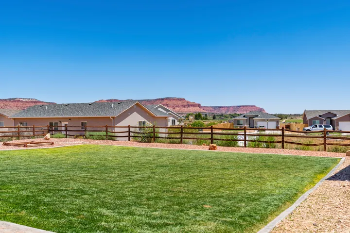 Expansive grassy yard with a split rail fence and distant natural rock formations