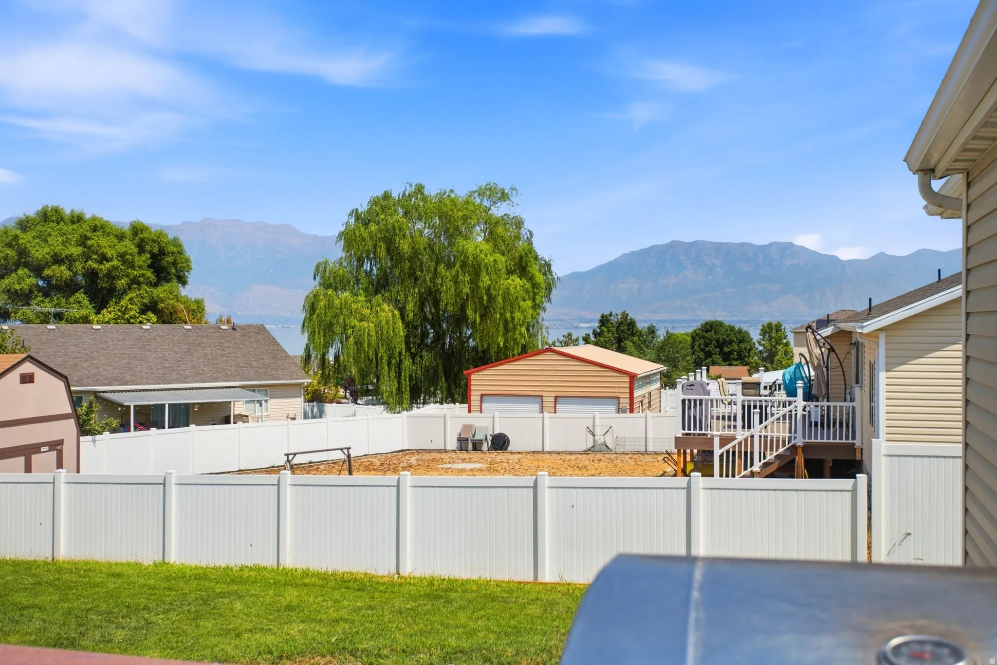 Expansive backyard space with a white vinyl fence and a detached structure featuring a dual garage door
