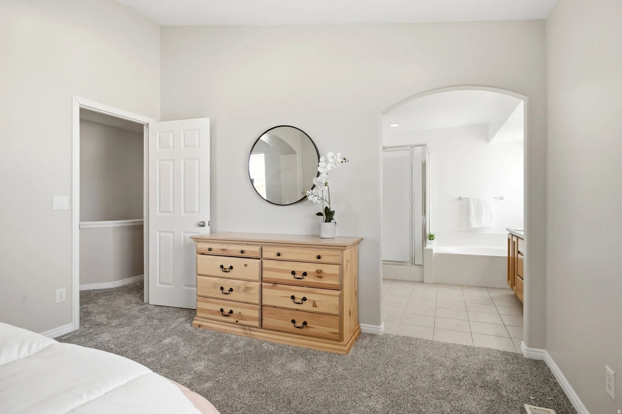 Primary Suite Carpeted bedroom with a walk-in closet, an arched entryway to a bathroom, a built-in shower with clear glass enclosure, a built-in tub, and tile flooring