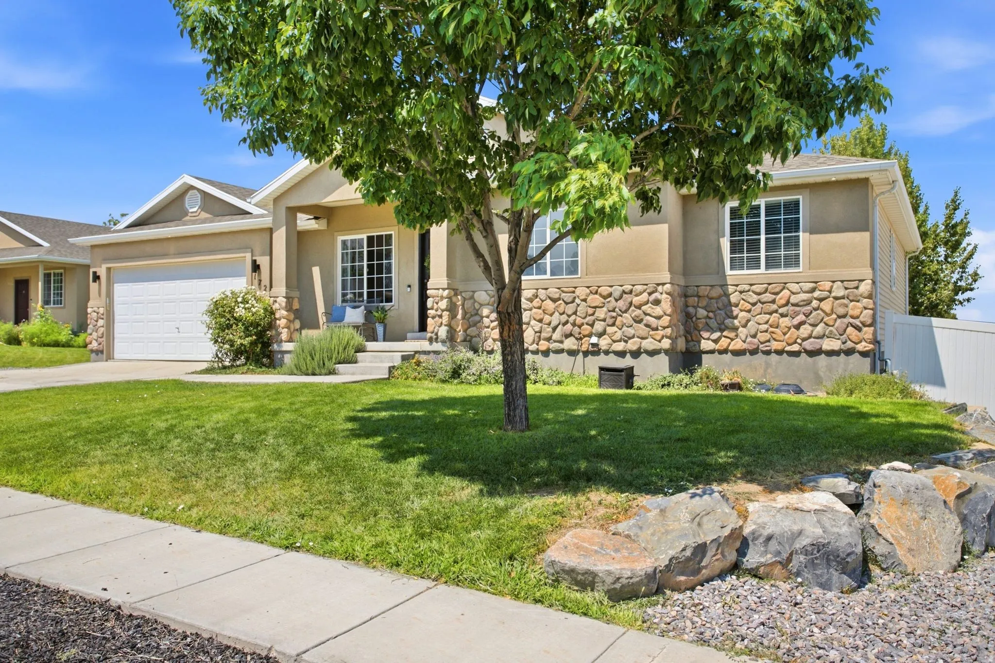 Contemporary stucco exterior with stone accents, an attached garage, and a concrete driveway