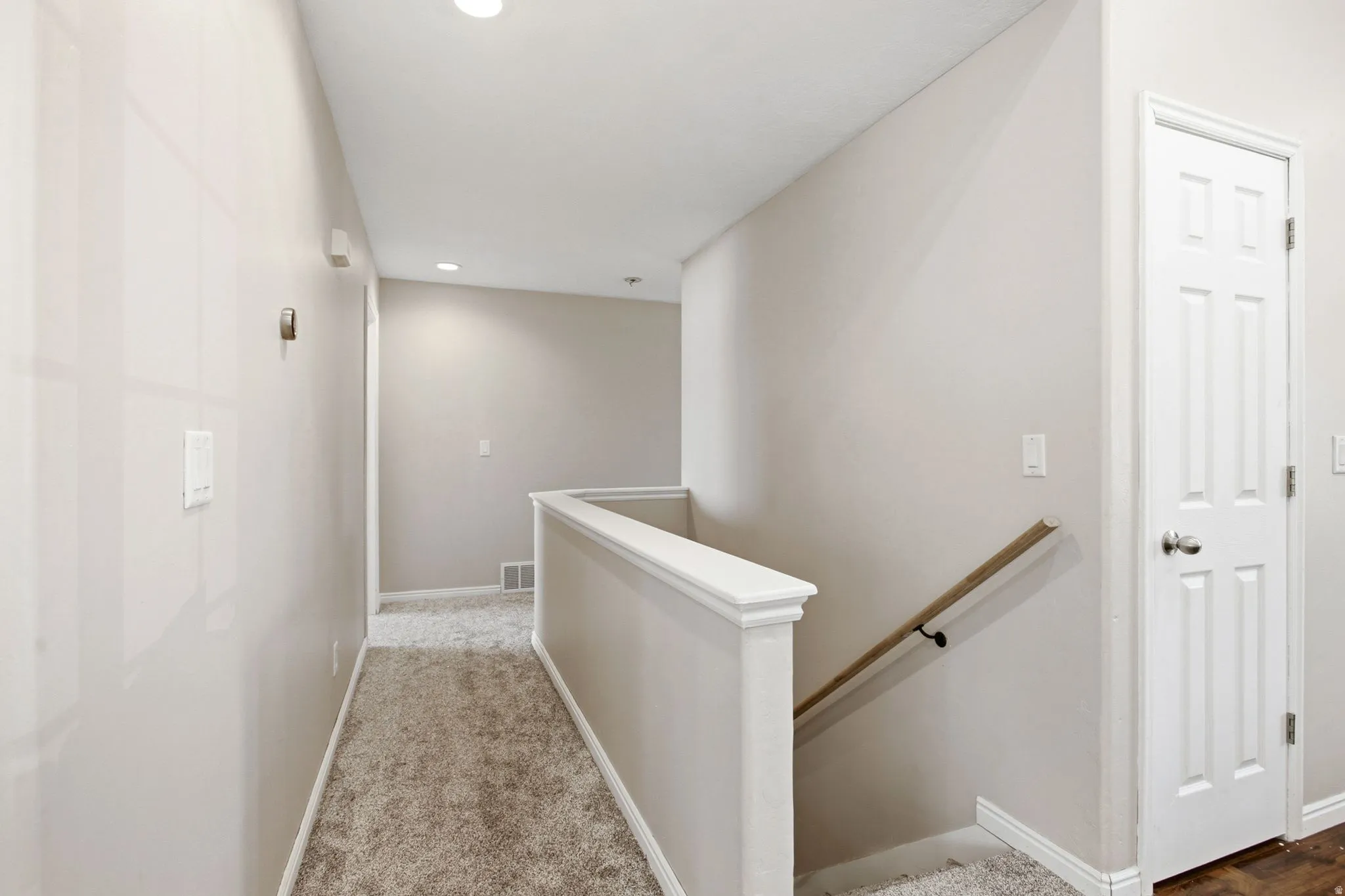 Carpeted hallway with recessed lighting and a paneled door
