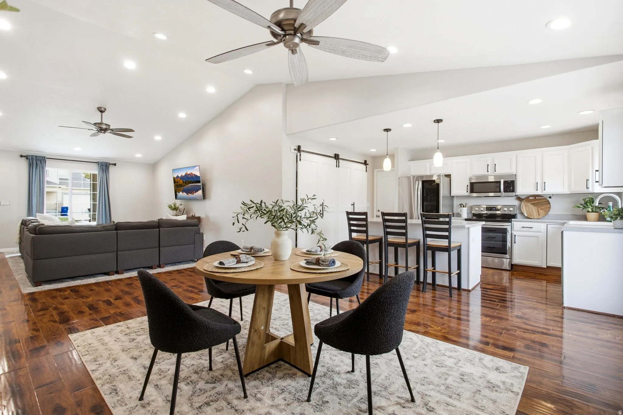 Open-concept floor plan featuring wood-finish flooring, vaulted ceilings with recessed lighting, and ceiling fans
