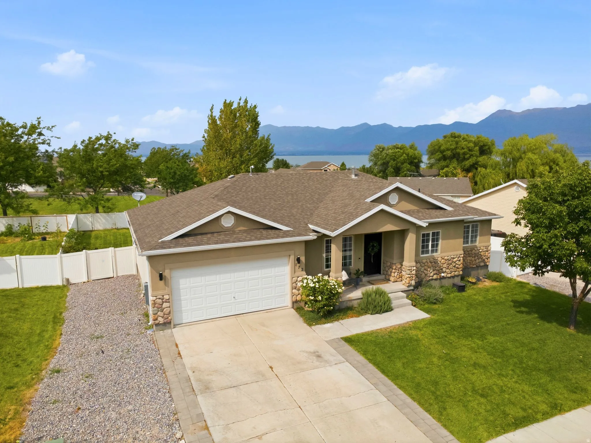 Stucco and stone exterior, attached two-car garage, concrete driveway, front yard with mature landscaping, and mountain backdrop