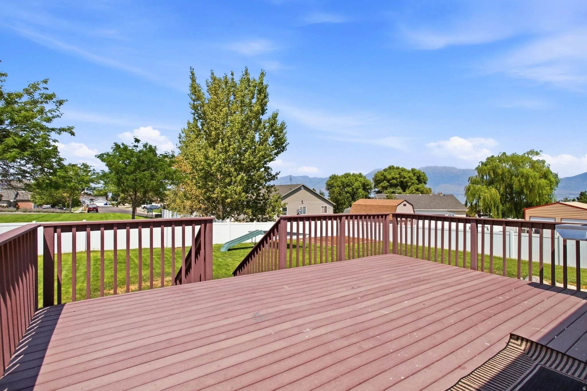 Expansive composite deck with a full railing and steps, overlooking a fenced yard and mature landscaping