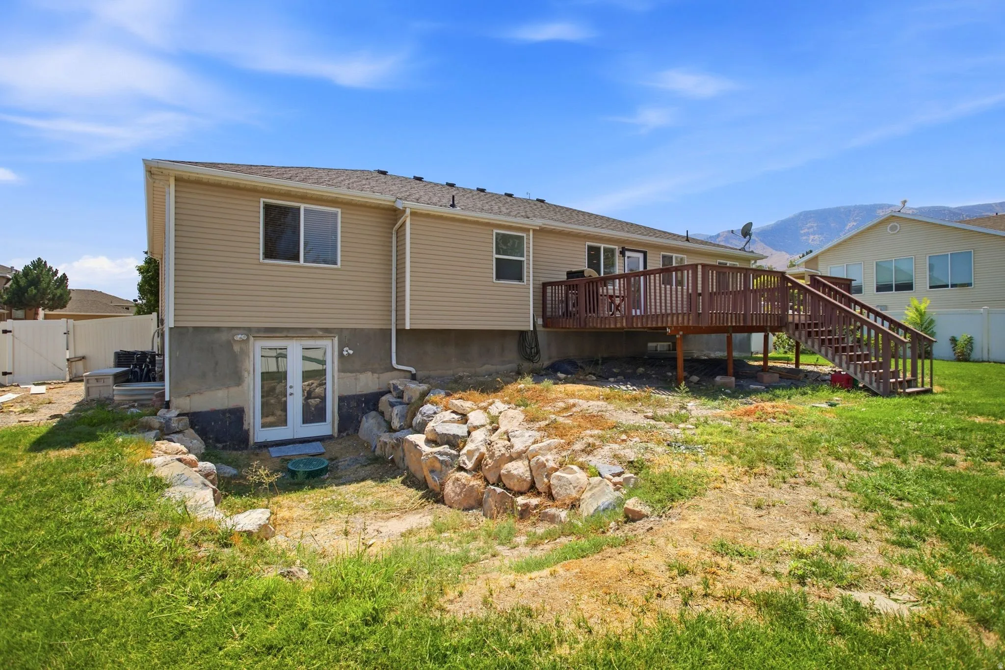 Expansive rear exterior featuring a raised wood deck with staircase, ground-level double french doors, and a partial mountain backdrop