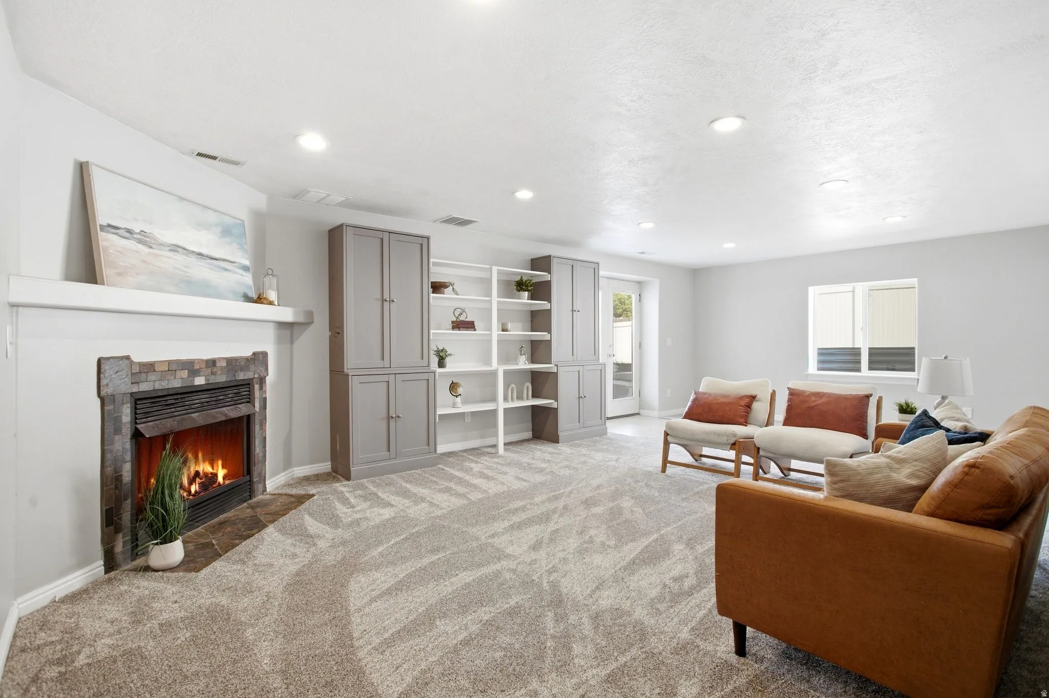Stone-surround fireplace with hearth, built-in shelving, built-in cabinetry, and recessed lighting