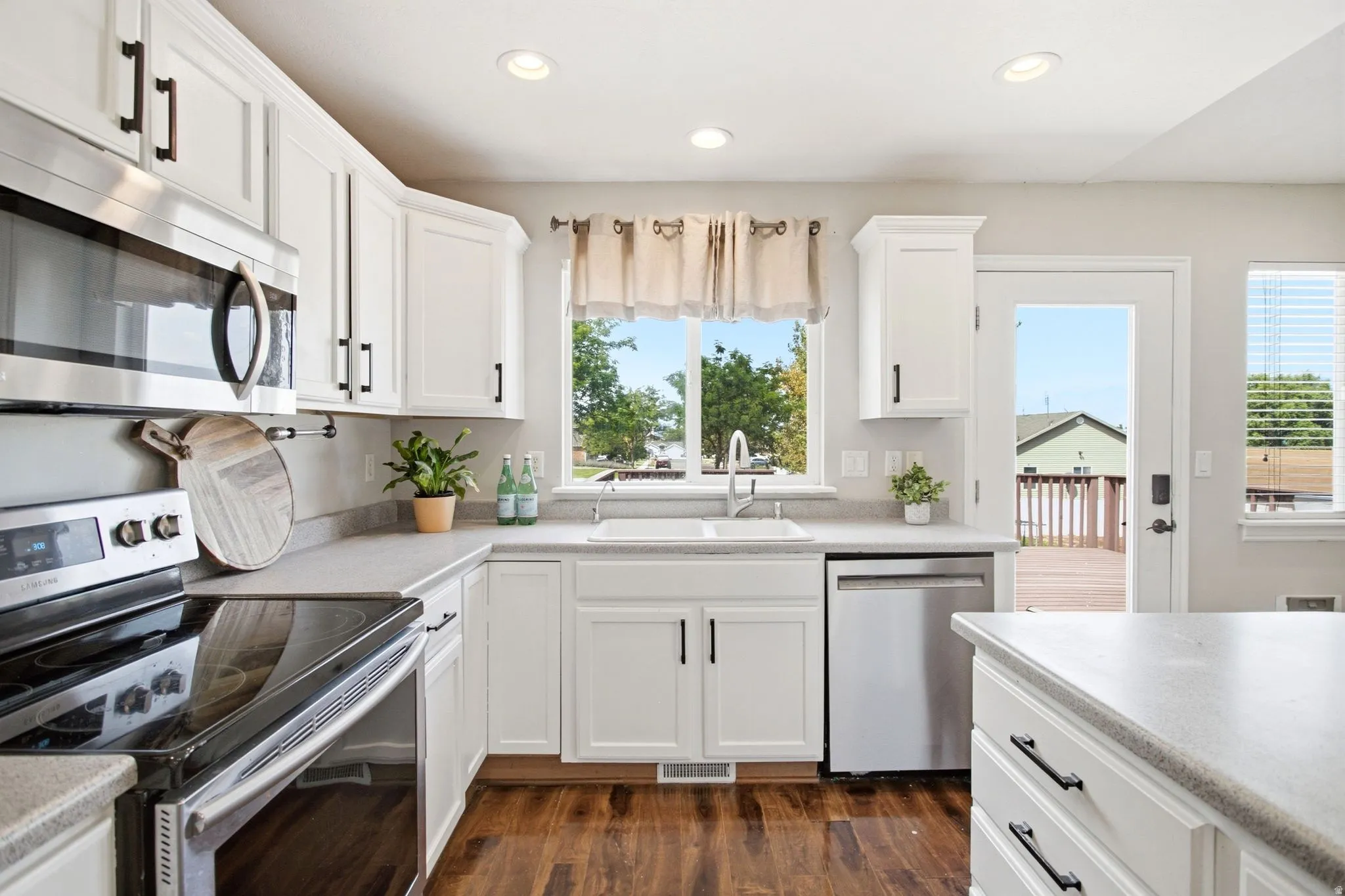 White shaker cabinetry, stainless steel appliances, wood-finish flooring, recessed lighting, and a glass-paneled exterior door