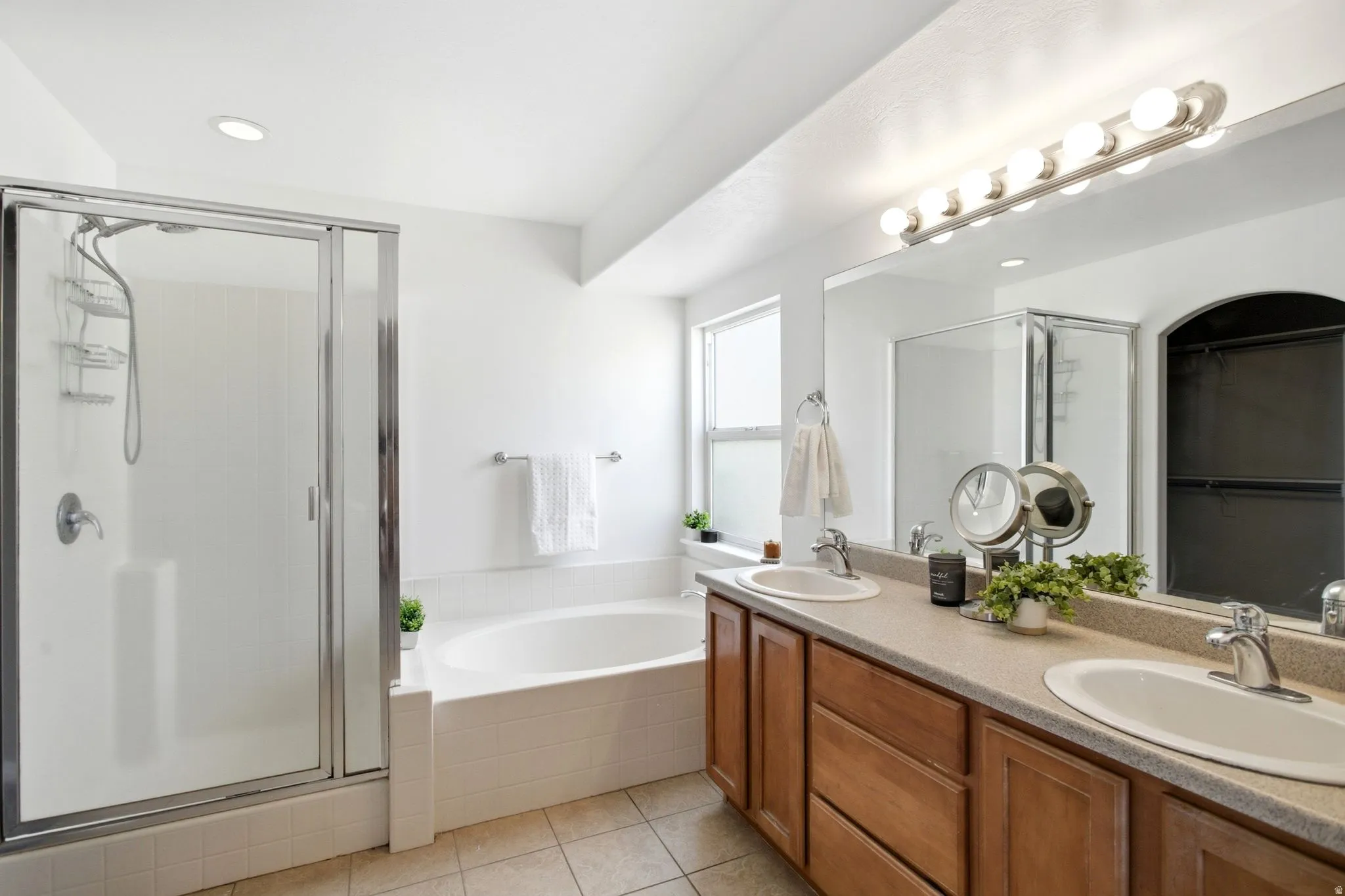 Primary suite Dual vanity with integrated sinks, wood-finish cabinetry, a large frameless mirror, and overhead strip lighting