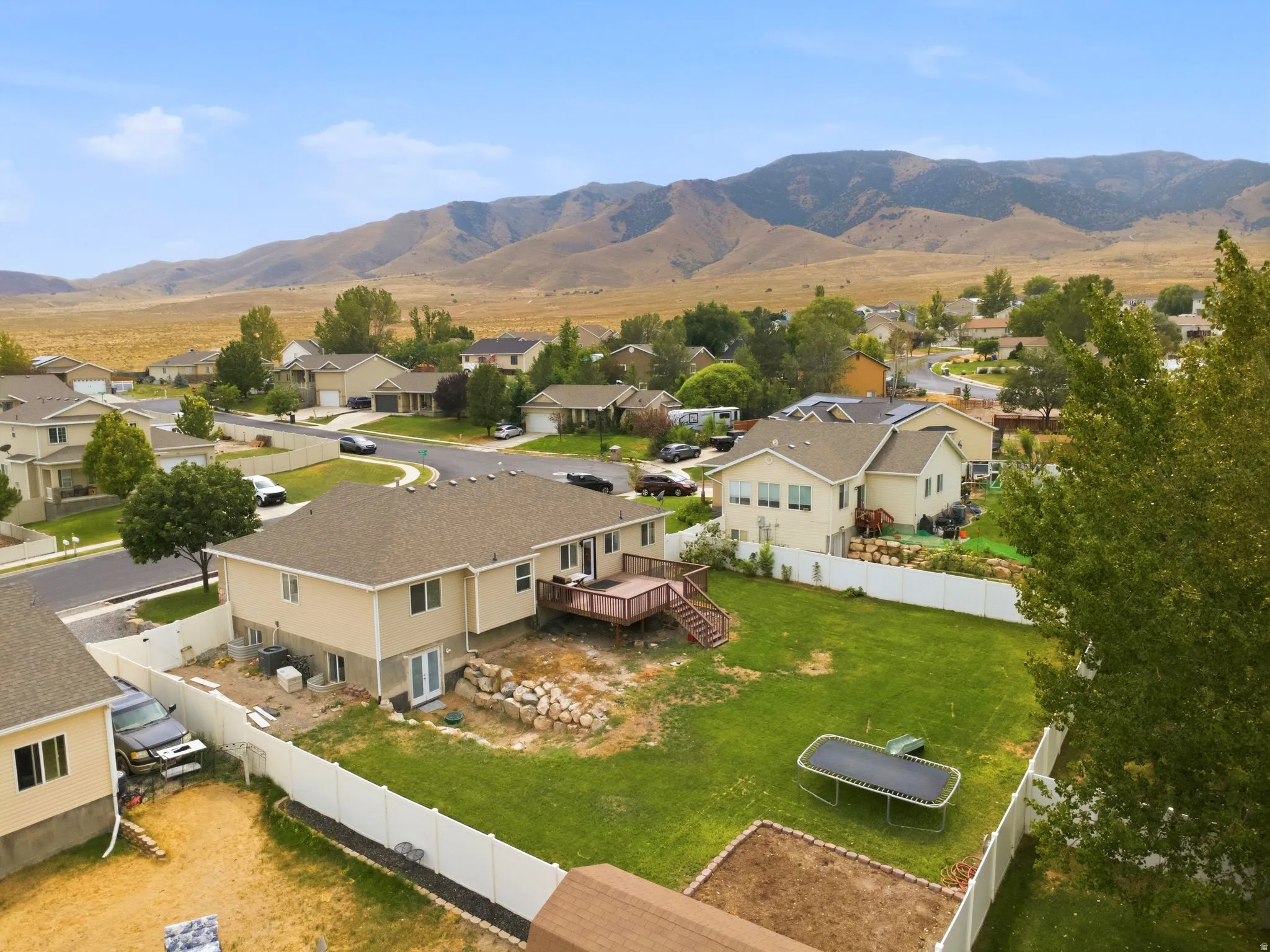 Expansive backyard featuring a manicured lawn, multi-level wood deck, and white privacy fencing