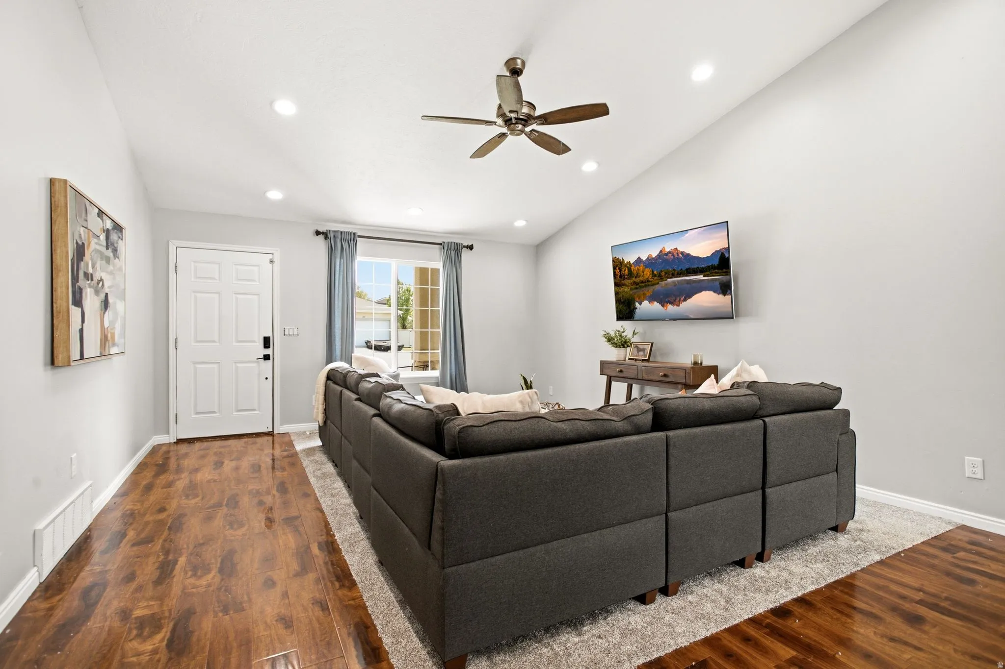 Vaulted ceilings with recessed lighting, wood-finish flooring, ceiling fan, white paneled entry door, and a large window with natural light