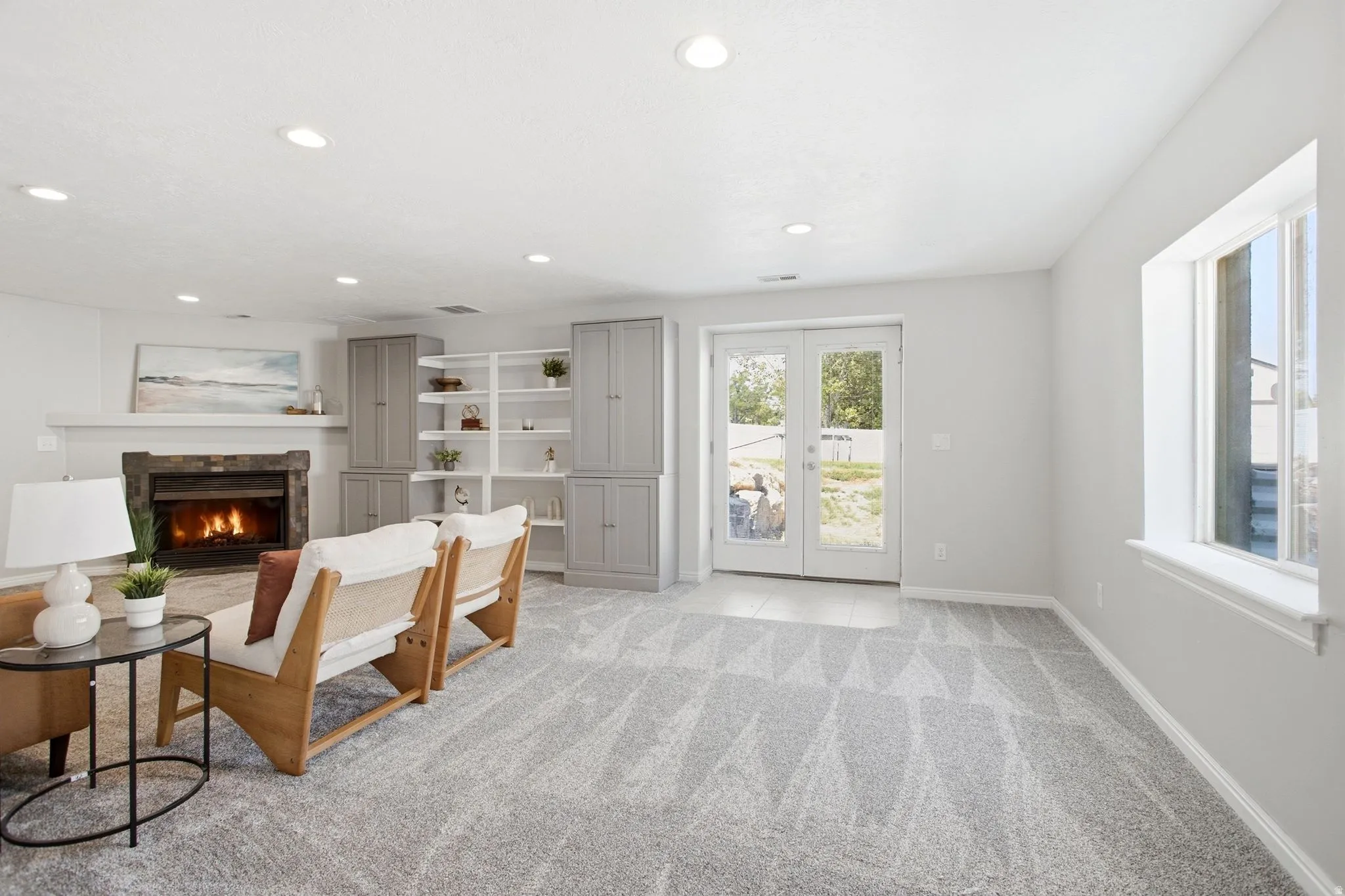 Recessed lighting, built-in shelving, glass-paned French doors, stone-clad fireplace, and neutral carpeting