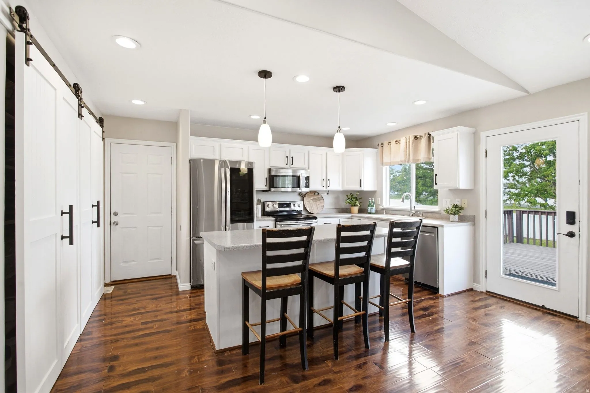 White kitchen featuring stainless steel appliances, wood-finish flooring, a full-lite exterior door, and a kitchen island with pendant lighting