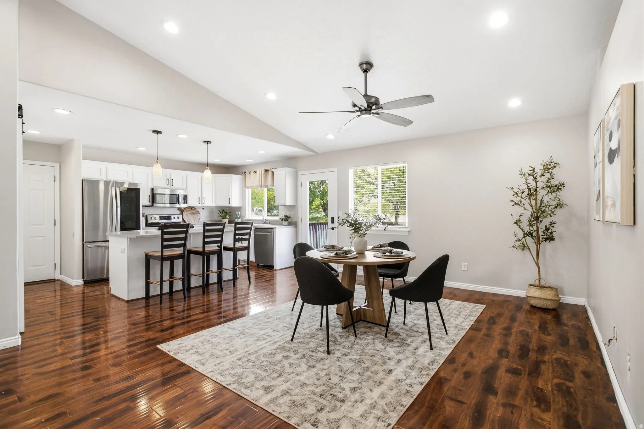 Vaulted ceilings with recessed lighting, wood-finish flooring, white kitchen cabinetry with stainless steel appliances, and a kitchen island with seating