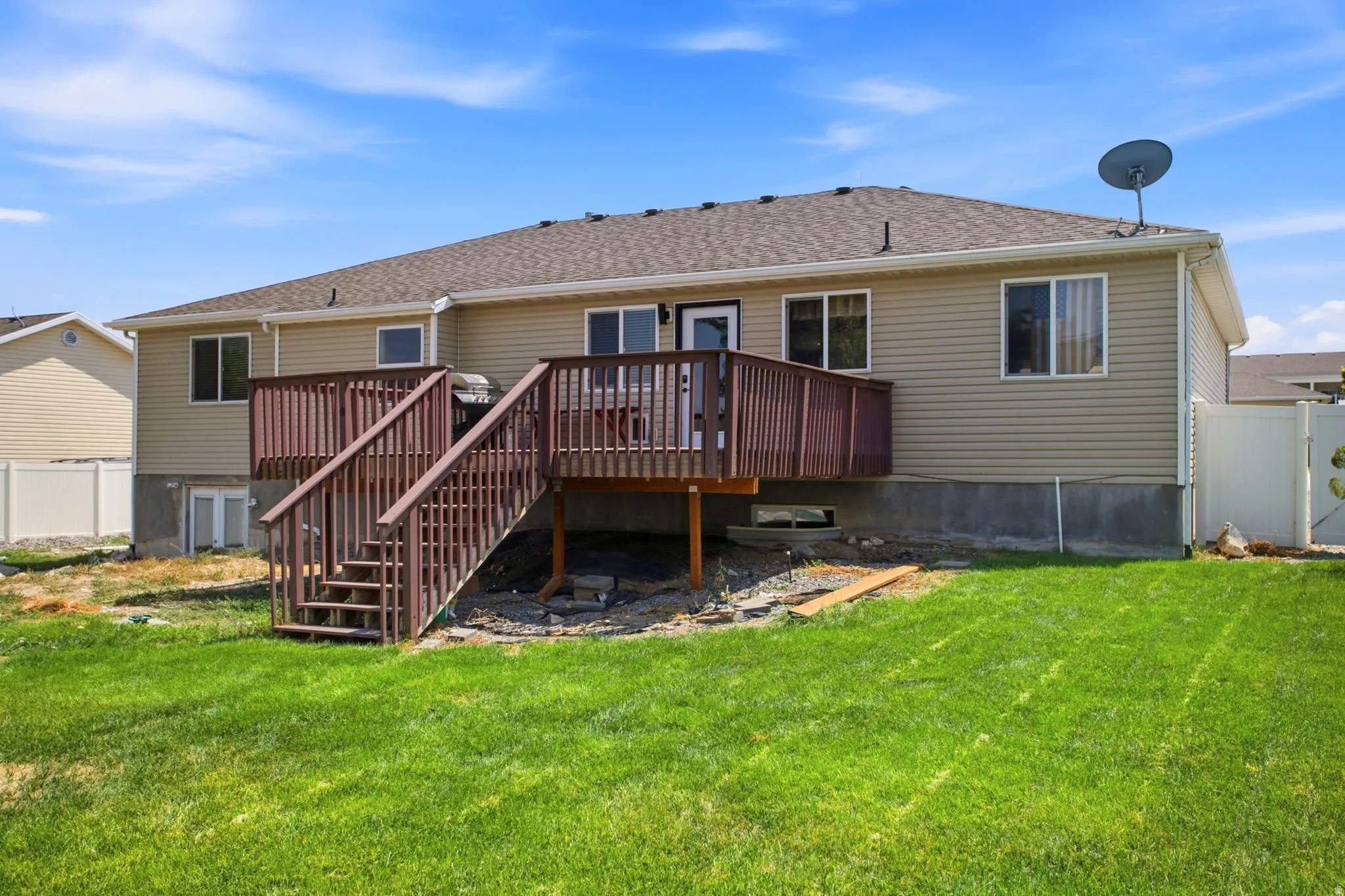 Expansive backyard featuring a manicured lawn, a two-story wooden deck with railings and stairs, and beige siding