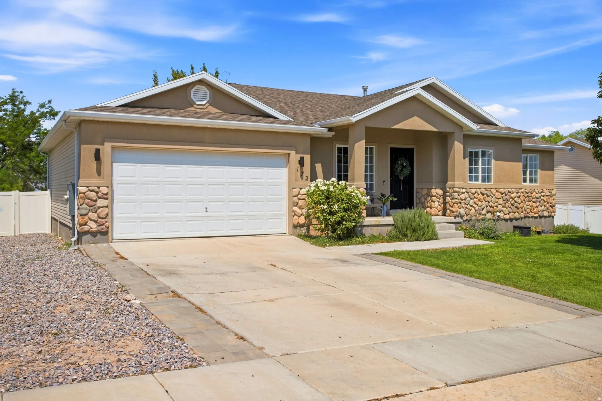 Tan stucco exterior with stone accents, a white garage door, and a concrete driveway