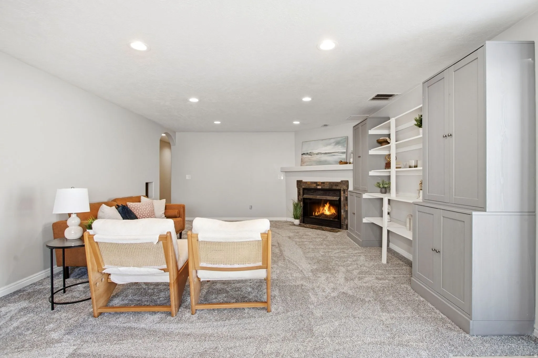 Recessed lighting illuminates the open living space, featuring a fireplace with stone surround and mantle