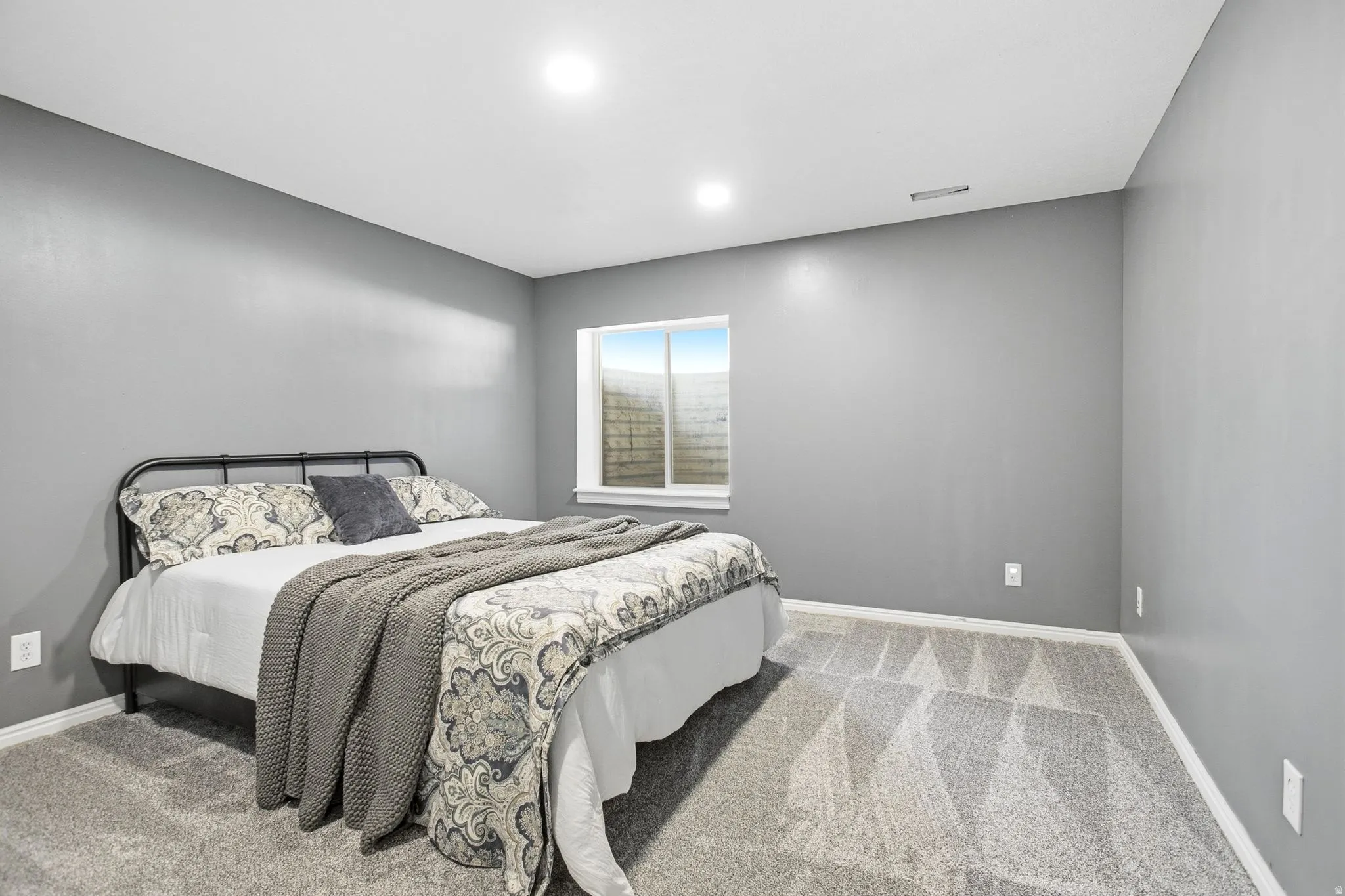 Recessed ceiling lighting, gray wall finish, window with white trim, and patterned carpeting