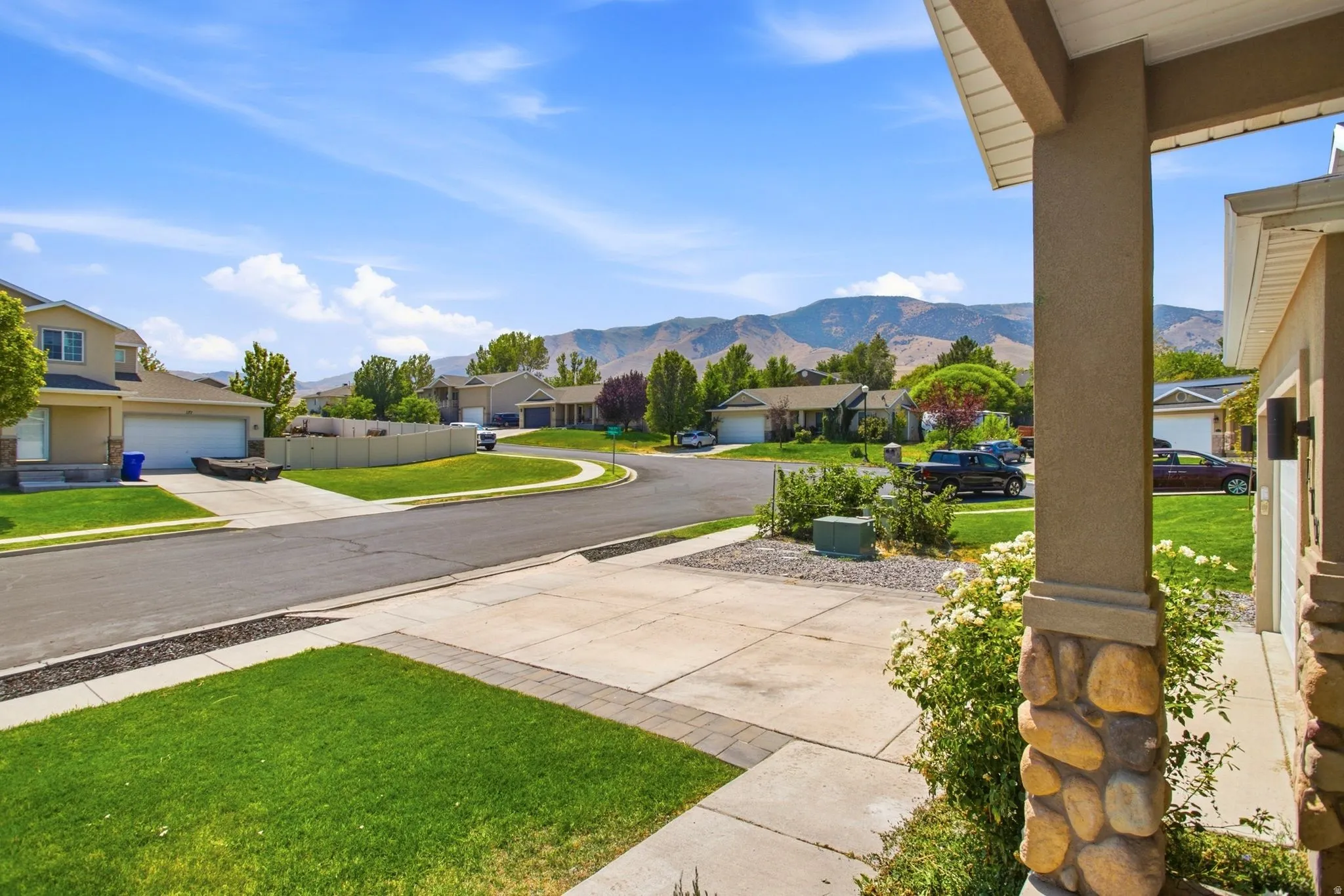 Stone-clad porch columns, landscaped front yard, paved driveway, mountain backdrop, and cul-de-sac street