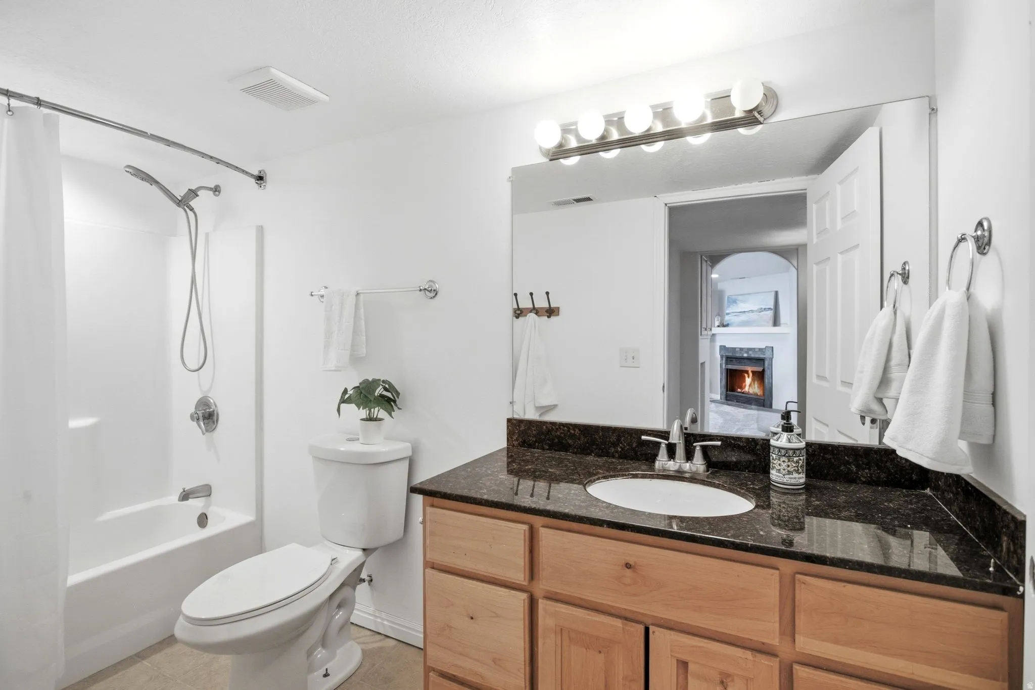Full bathroom with a tub/shower combination, single vanity with dark countertop, light wood-finish cabinetry, and a wall-mounted light fixture