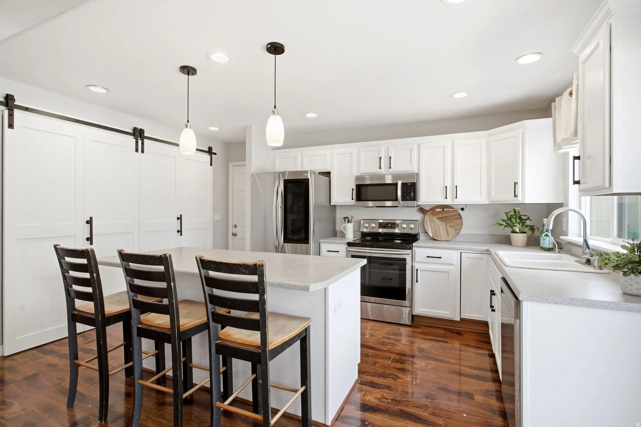 Spacious kitchen featuring white cabinetry, stainless steel appliances, a center island with counter seating, wood-finish flooring, and barn door accents
