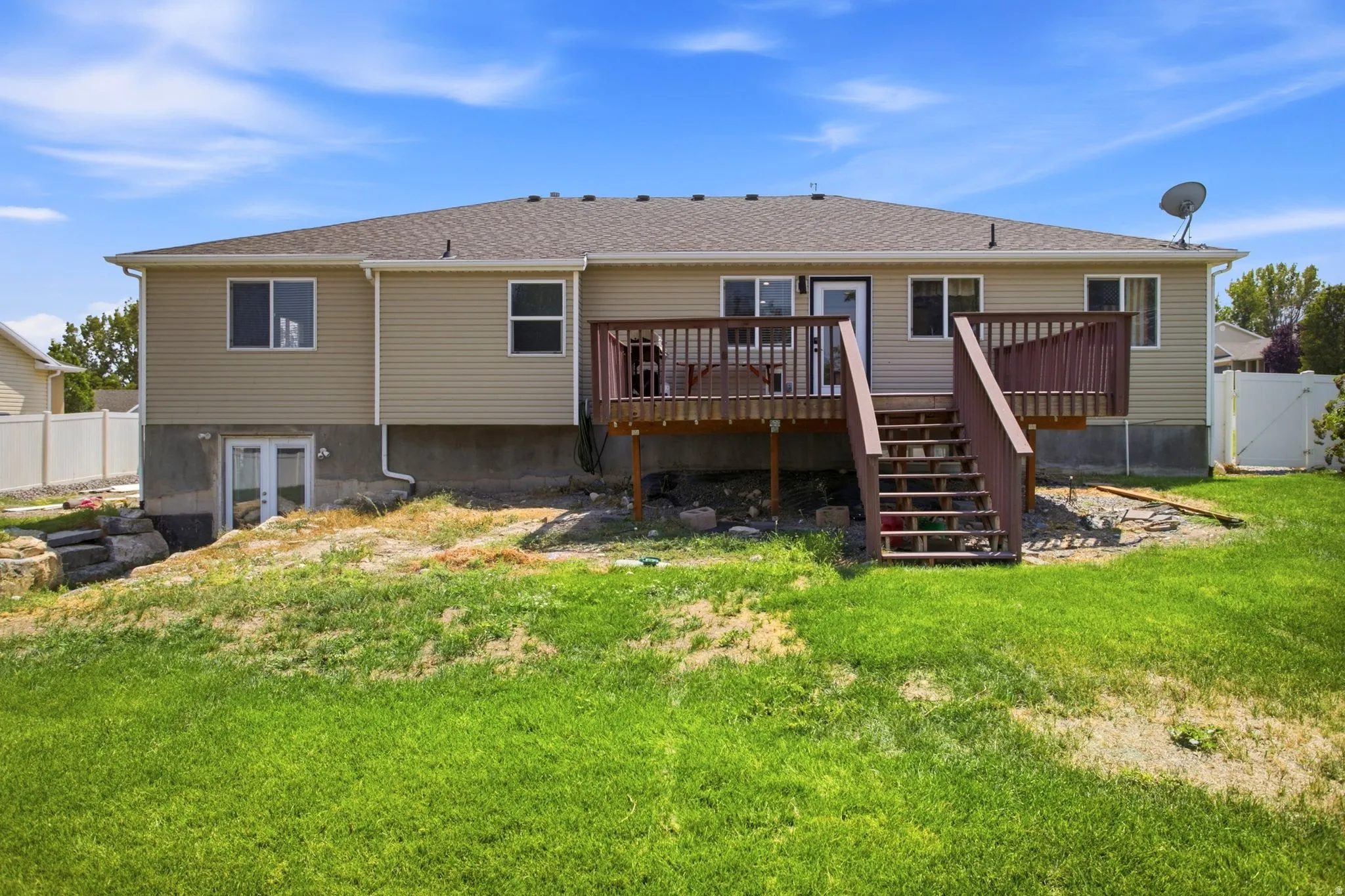 Rear exterior featuring a wood-finish deck with stairs, beige siding, and multiple windows