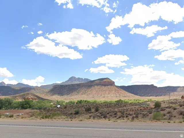 Expansive desert landscape with mountainous terrain, distant green vegetation, and a clear blue sky