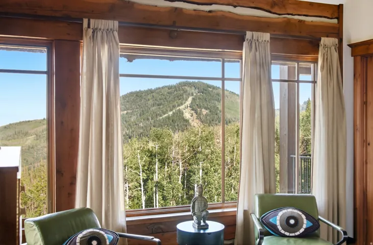 Expansive windows with wood trim, natural wood ceiling beams, and mountain scenery