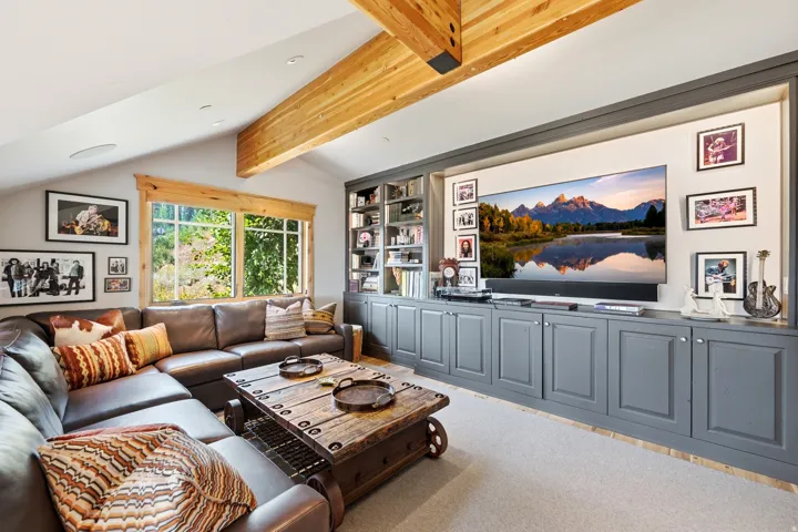 Built-in media console with storage, integrated shelving, exposed wood beams, and large picture windows