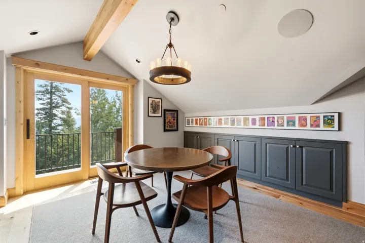 Vaulted ceiling with exposed beam, natural wood-frame sliding glass doors, built-in cabinetry with panel doors, recessed lighting, and a drum chandelier