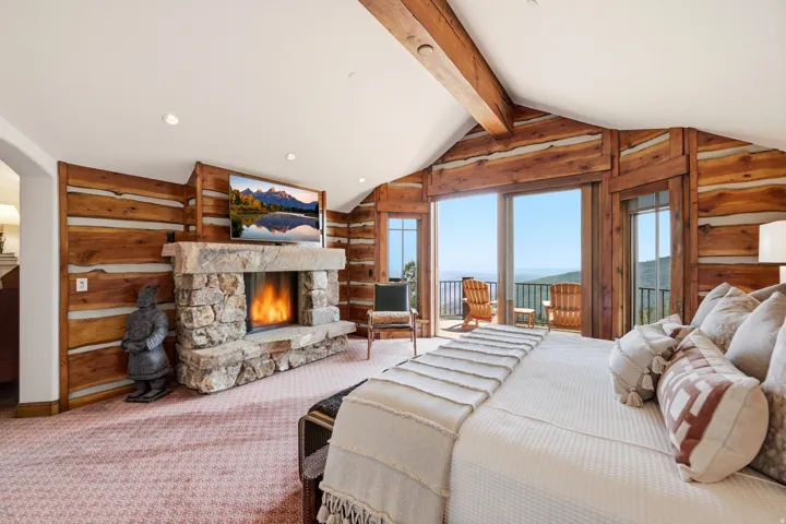 Stone fireplace with a mantle, wood-paneled walls, vaulted ceiling with exposed wood beams, and a sliding glass door leading to a balcony