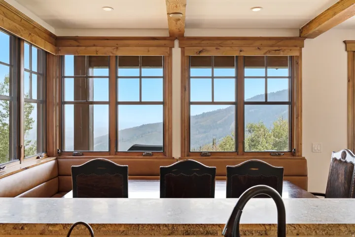 Built-in banquette seating with upholstered cushions, wood-framed windows, and exposed wood ceiling beams