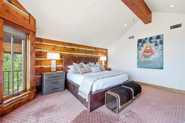Vaulted ceilings with exposed wood beams, log wall detailing, integrated recessed lighting, and a large window with a metal balcony railing