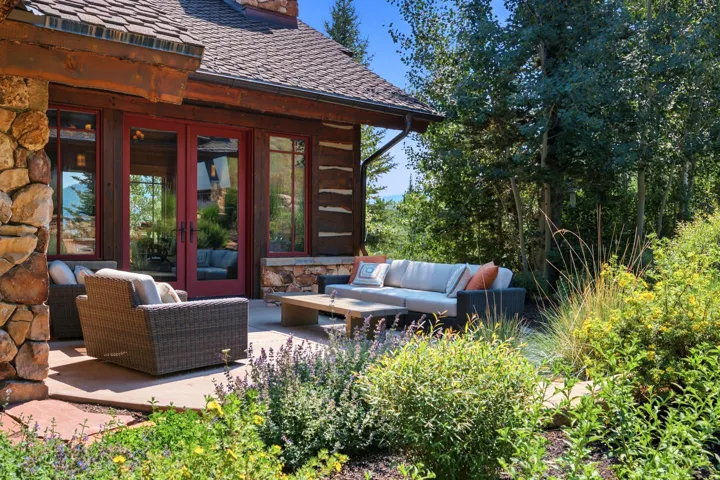 Stone exterior wall, wood-paneled exterior, red-framed glass doors, concrete patio, mature trees