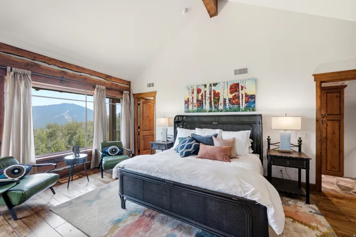 Vaulted ceiling with exposed wood beams, expansive window framing mountain scenery, wood-finish flooring, built-in wooden cabinetry, and a dark metal bed frame