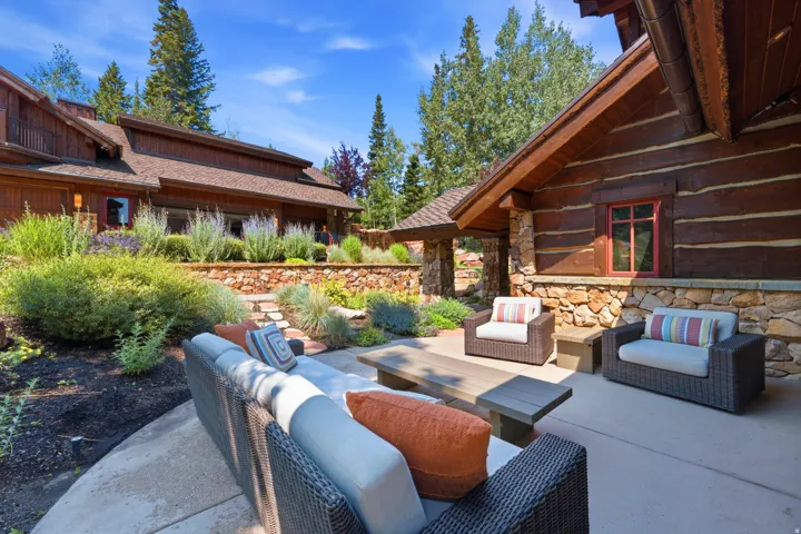 Expansive outdoor patio with concrete flooring, accented by a stone base and log siding