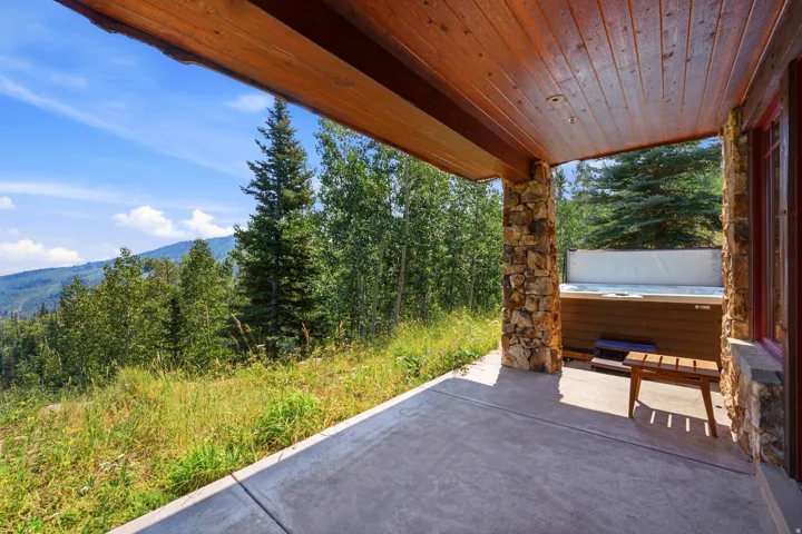 Covered outdoor patio with a built-in hot tub, concrete flooring, and natural stone pillars
